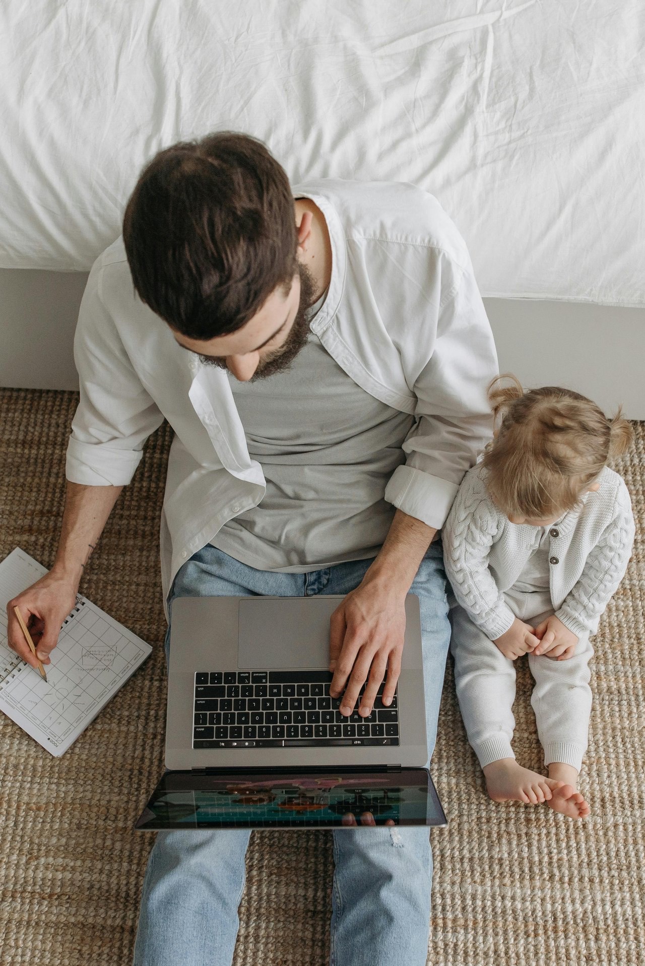 A father working on a laptop with his young daughter on his lap